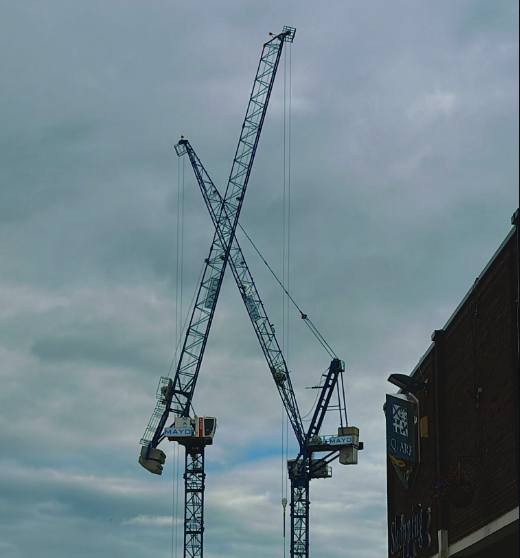 Two crossed construction cranes against a grey sky